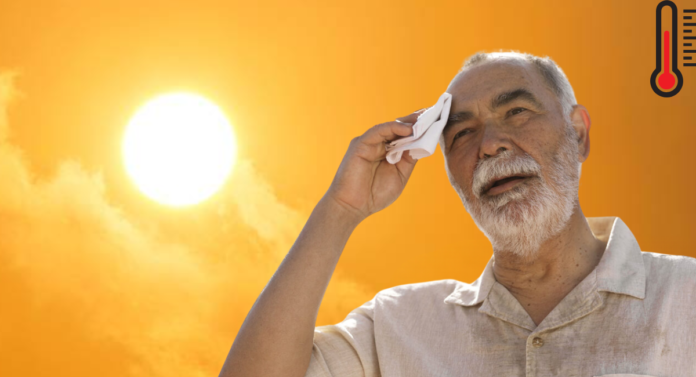 An elderly man wipes his forehead with a cloth, squinting in the bright sunlight against a vivid orange sky.