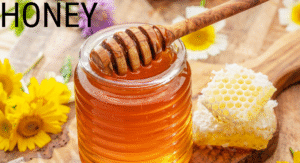 Foods Not to Refrigerate: 15 items That your Storing Wrong 10 A jar of golden honey with a wooden dipper, accompanied by honeycomb, surrounded by yellow flowers on a wooden surface.