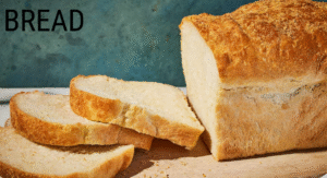 Foods Not to Refrigerate: 15 items That your Storing Wrong 7 Loaf of freshly baked bread with several slices cut, resting on a wooden surface against a textured blue background.