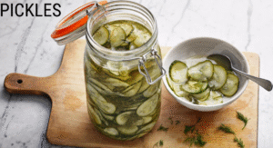 Foods Not to Refrigerate: 15 items That your Storing Wrong 9 A jar of dill pickles sits on a wooden board beside a bowl of sliced pickles, garnished with fresh dill.