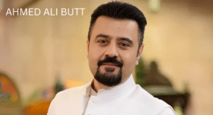 Love Guru Cast Spotlight: Mahira Khan, Humayun Saeed and More 3 Ahmed Ali Butt, in a white traditional outfit, poses in a stylish, blurred indoor setting.