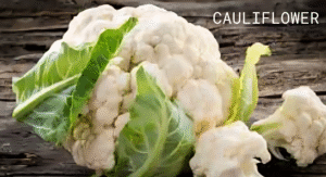 Top Foods That Increase Uric Acid & Effect Your Health: Try Their Alternatives 4 A fresh cauliflower with green leaves rests on a rustic wooden background, showcasing its vibrant color and texture.