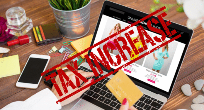 A laptop displays a fashion shopping website, while a hand holds a credit card amid various colorful stationery supplies.