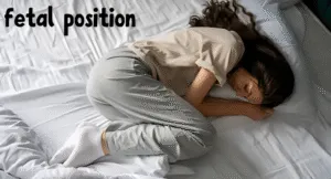 Best Sleeping Positions to Improve Sleep Quality for Healthy Lifestyle 1 A woman sleeps curled up in a fetal position on a bed, with her long hair draped over a white pillow. The room appears calm and quiet.
