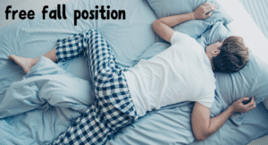 A person sleeping on their stomach in the "free fall" position, wearing plaid pajama pants and a white t-shirt on a blue bedspread.