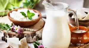 Top Foods That Increase Uric Acid & Effect Your Health: Try Their Alternatives 7 A glass jug of full fat milk beside bowls of cottage cheese and cream, with fresh herbs and flowers on a wooden table.