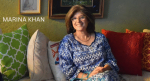 Love Guru Cast Spotlight: Mahira Khan, Humayun Saeed and More 5 Marina Khan, in blue patterned attire, sits comfortably on a couch surrounded by colorful cushions and decorative wall art.
