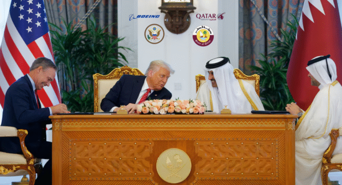 U.S. and Qatari officials engage in a signing ceremony, surrounded by national flags and decorative elements, with flowers on the table.