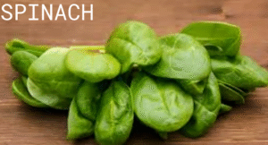 Top Foods That Increase Uric Acid & Effect Your Health: Try Their Alternatives 3 A fresh bunch of green spinach leaves arranged on a wooden surface, highlighting their vibrant color and crisp texture.
