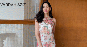 Love Guru Cast Spotlight: Mahira Khan, Humayun Saeed and More 11 Vardah Aziz stands confidently in a floral dress by Vardah Aziz, showcased against a warm wooden backdrop with bright natural light.