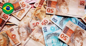 Top 13 Most Beautiful Banknote Designs Around the World 3 A close-up view of various Brazilian banknotes, featuring denominations of 50 and 100 reais scattered on a surface, with a Brazil flag icon.