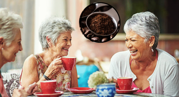 Three elderly women sip coffee from red cups while seated around a patterned table, chatting in a cozy setting. Coffee grounds are inset.