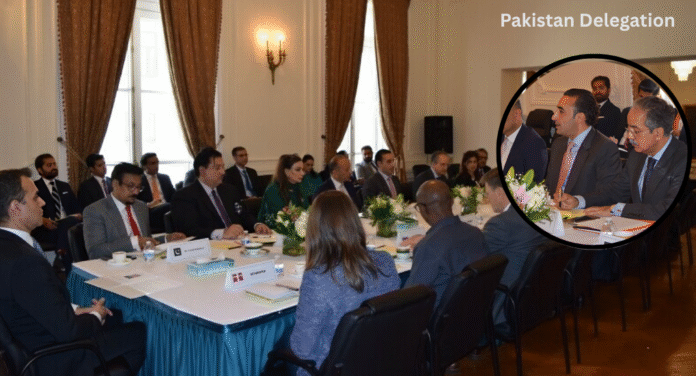 A formal meeting with a diverse group of people seated around a conference table, decorated with flowers and stationery, in a well-lit room.