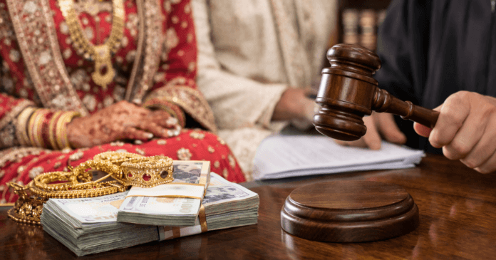 A gavel is held above a table with gold jewelry and stacks of cash, while two individuals in traditional attire observe.